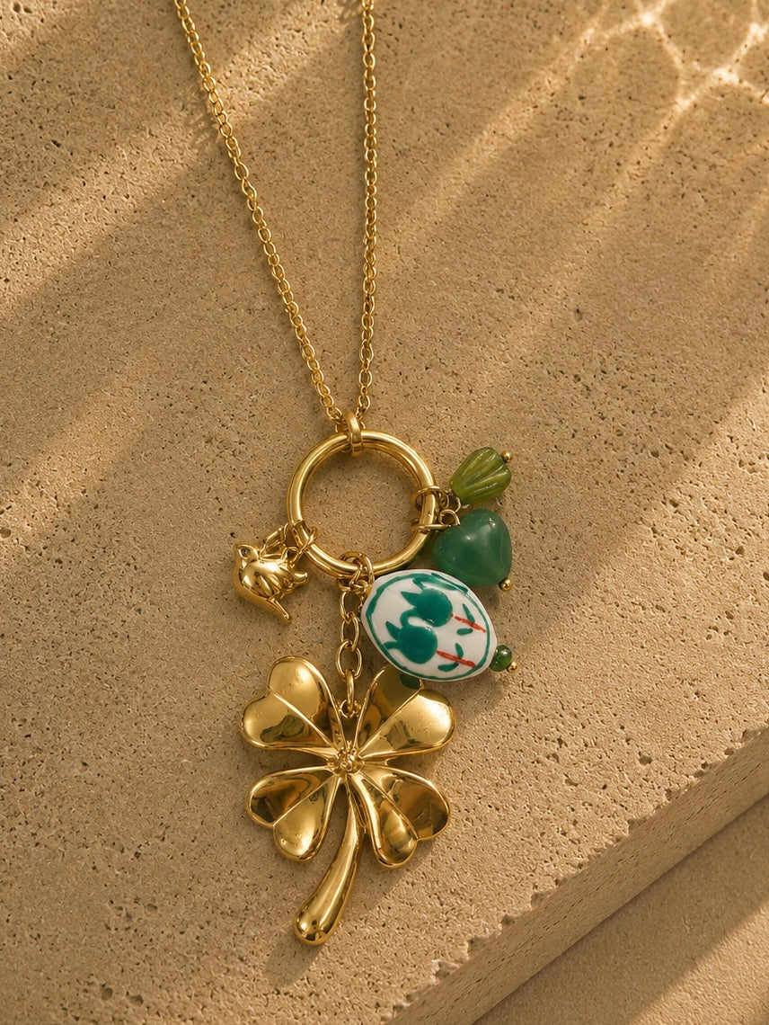 Détail collier charms trèfle et médaillon doré – trèfle bombé, oiseau doré, médaillon porcelaine chinoiserie et aventurine verte – Bijoux Incandescence