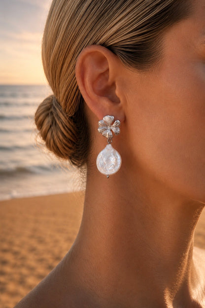 Boucles d'oreilles fleur et perle goutte nacrée argentées portées – puce hibiscus finement striée en relief et grande perle baroque irisée, ambiance bord de mer – Bijoux Incandescence