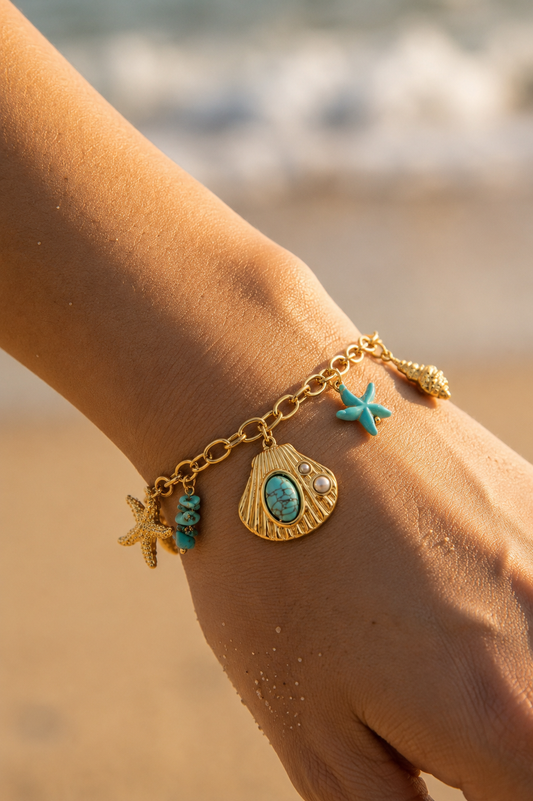 Bracelet charms mer turquoise doré porté au poignet – coquille dorée, pierre turquoise, étoile de mer et perles – Bijoux Incandescence