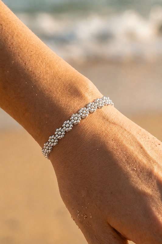Bracelet jonc argenté porté au poignet sur fond de plage — grandes fleurs en perles argentées en relief en acier inoxydable — Bijoux Incandescence