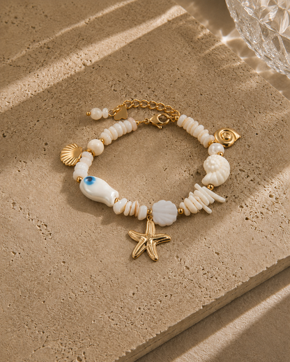Bracelet trésor marin – perles nacre blanche variées avec charms étoile de mer dorée, coquillages nacrés, escargot et perle œil bleu, style bord de mer luxe – Bijoux Incandescence