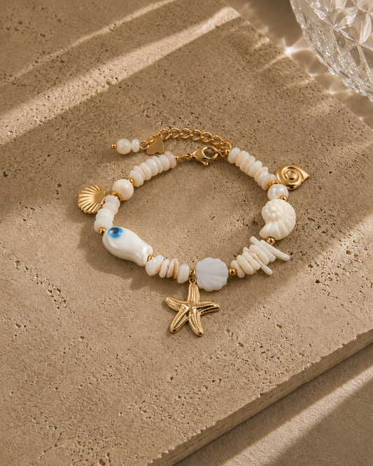 Bracelet trésor marin – perles nacre blanche variées avec charms étoile de mer dorée, coquillages nacrés, escargot et perle œil bleu, style bord de mer luxe – Bijoux Incandescence